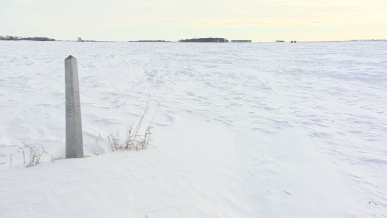 Small concrete obelisk sticks up in a snow-covered field.