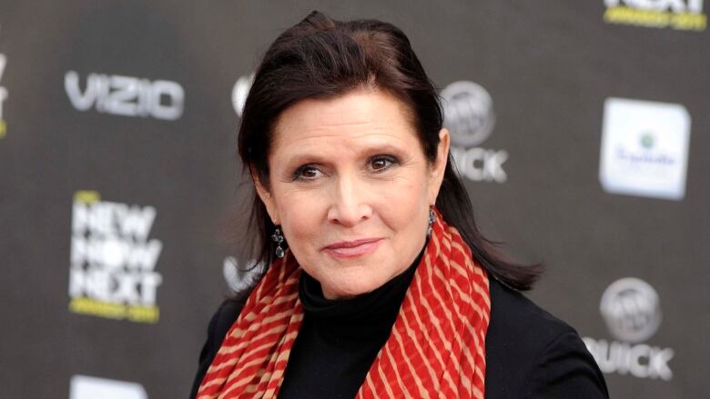 Actor Carrie Fisher wears a black top and red and gold scarf.