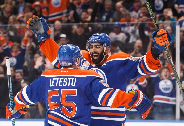 Two hockey players in Edmonton Oilers home sweaters share a celebratory hug.