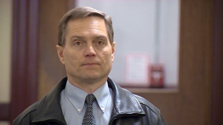 A man in a leather jacket and shirt and tie is shown.