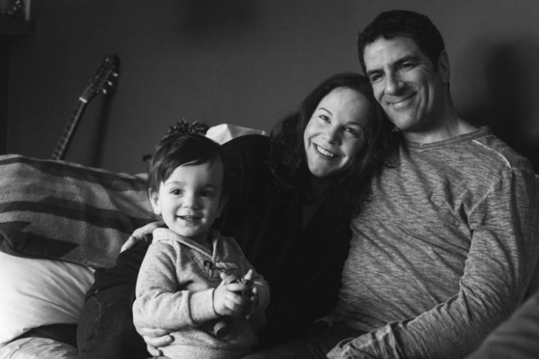 A mother and father, with a smiling male baby, in a black-and-white picture.