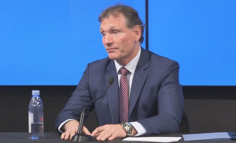 Man in a suit and tie sits in front of a microphone