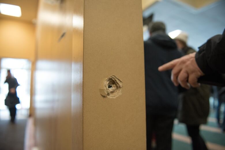 A person points to a bullet lodged in the column of a building. 