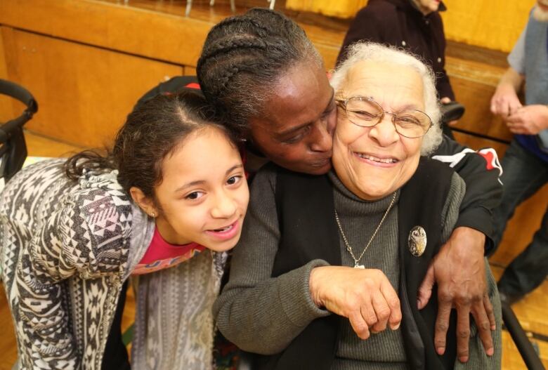 Three people with the middle person kissing the person on the right on the cheek