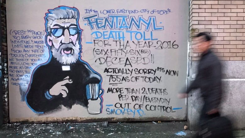 A man walks past a graffiti mural of a preacher with facts about the toxic drug crisis written beside his image.