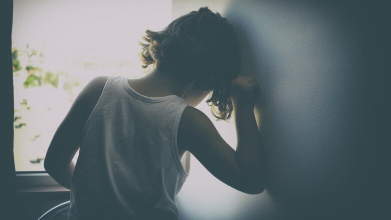 A child leans his forehead and forearm against a wall.