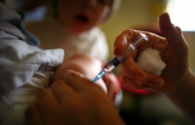 A close up of a hand giving a vaccine to a baby. 