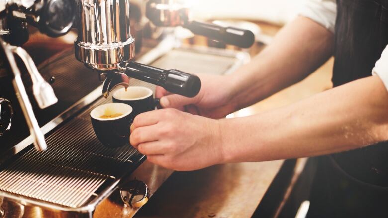 An espresso machine is pictured extracting coffee to two espresso cups held by a barista.