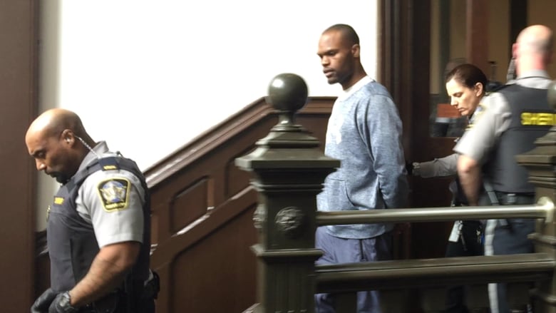 A man is escorted down the stairs of a courthouse by sheriffs.