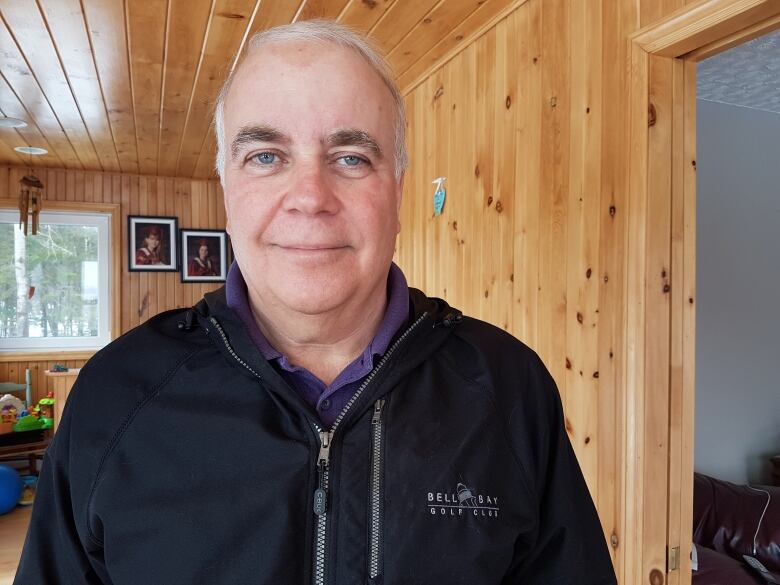 A man with grey hair in a pine wood pannelled room smiles for the camera.