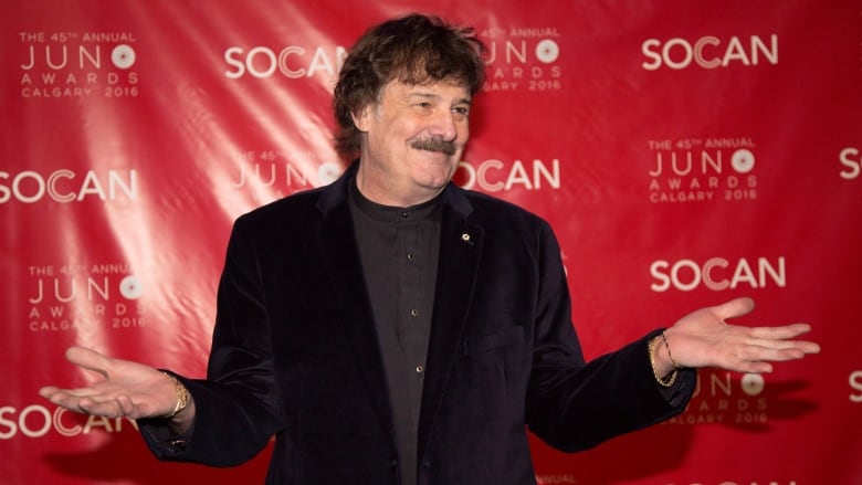 A man shrugs in front of a sponsored backdrop.