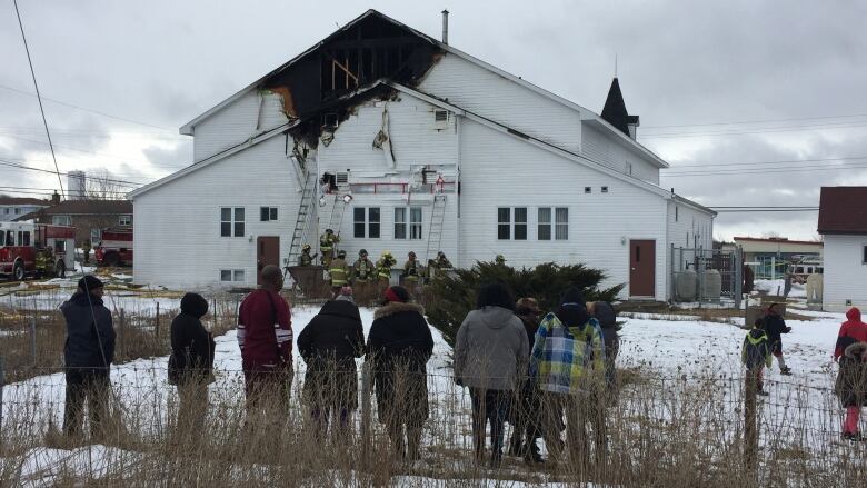  Passersby watch as firefighters continue to monitor a church fire.