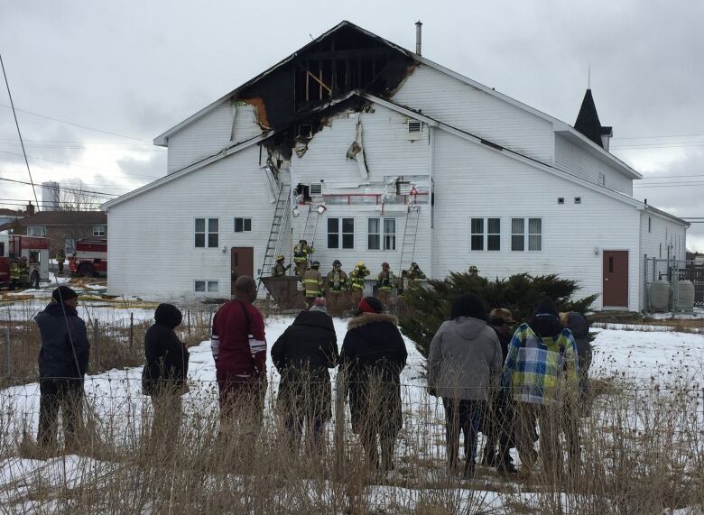  Passersby watch as firefighters continue to monitor a church fire.