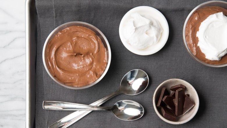 An overhead shot of a tray with small dishes of chocolate pudding, whipped cream, and chocolate pieces.