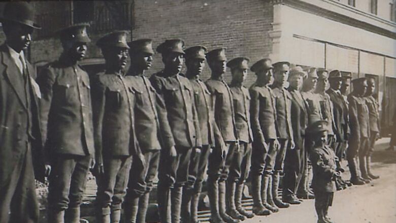 An old picture of a line of people in military uniforms and a young boy in a similar uniform