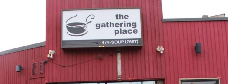 A red building with a black and white sign on it that reads 'the gathering place' 