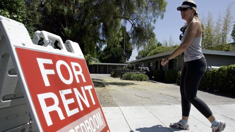 A woman walks past a 'For Rent' sign.