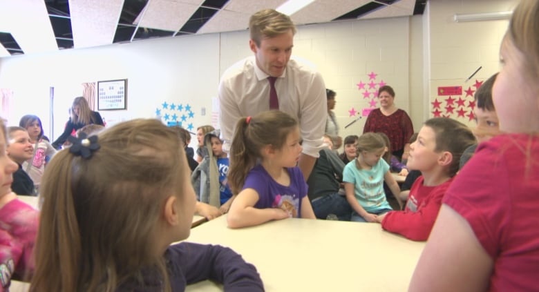 A man leans over to talk to a table of young children