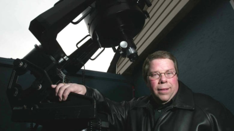 A man stands behind  a telescope