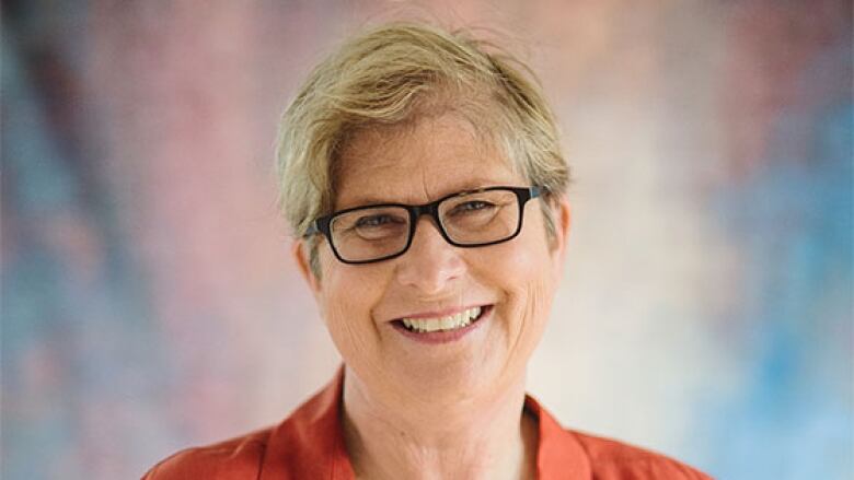 Smiling woman with short hair and glasses wearing an orange shirt against a non-descript background.