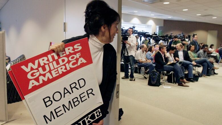 A woman holds a sign that reads Writers Guild of America Board board member on strike.