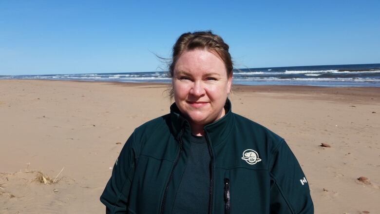 Woman in Parks Canada jacket standing on beach.