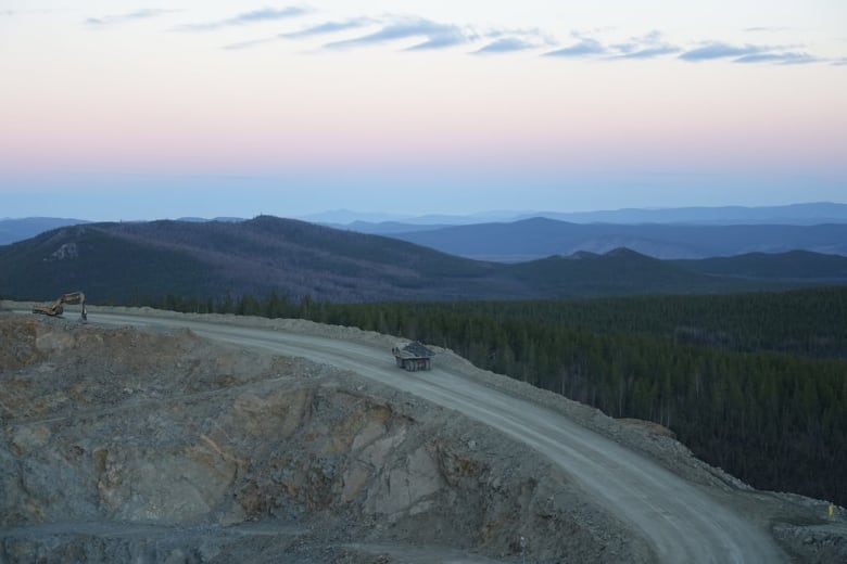 An ore truck is seen from above, driving on a remote road with mountains in the background.