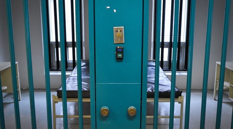 A pair of low beds with thin mattresses can be seen behind bars in two neighbouring jail cells.