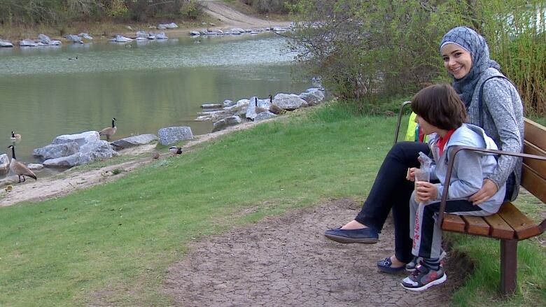 A woman and child sit on a bench watching Canada Geese