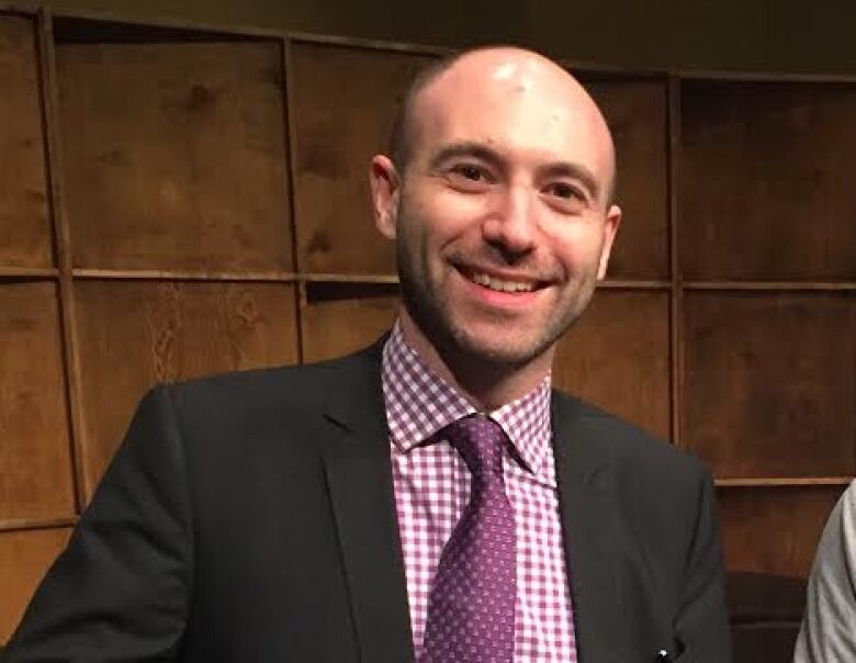 Man smiling in black suit and purple shirt.