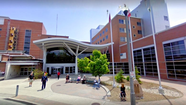 People walk and sit on benches in front of the entrance to Lakeridge Health hospital in Oshawa.