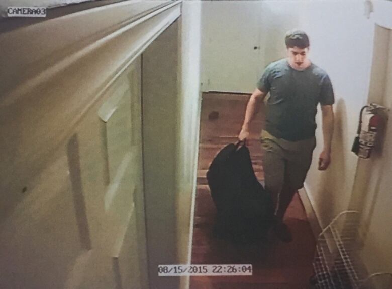 A man is seen walking down a hallway with a black duffel bag.