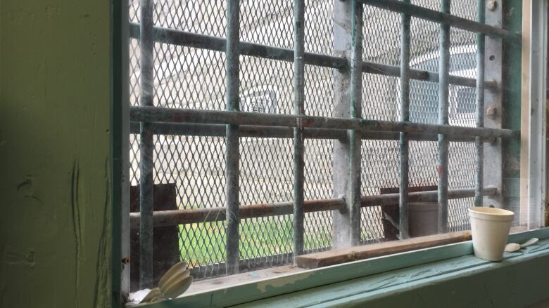 Dirty plastic spoons and a styrofoam cup sit on a dirty window ledge. Bars are on the window. 