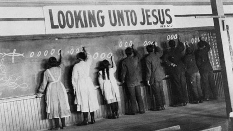 Children write at a chalkboard.