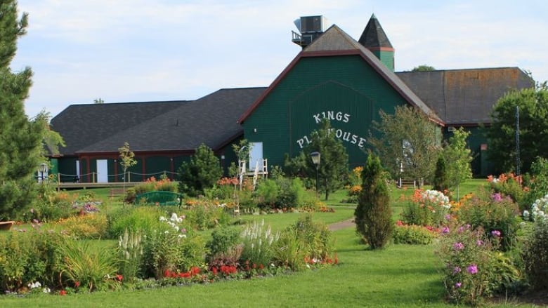 A lush green lawn and gardens with a green building in the back.