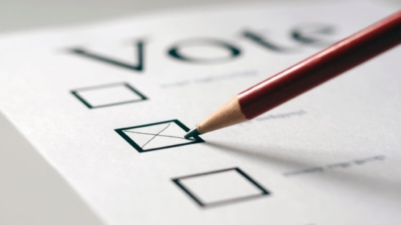 Close-up of a pencil marking an X in a box next to a blurred out name on a piece of paper labelled 