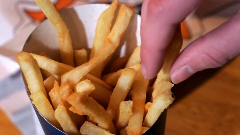 A close-up of a person reaching out to grab a french fry from a fast food container.