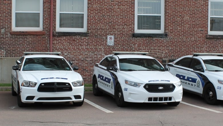 Three police cars are seen parked in front of a brick building