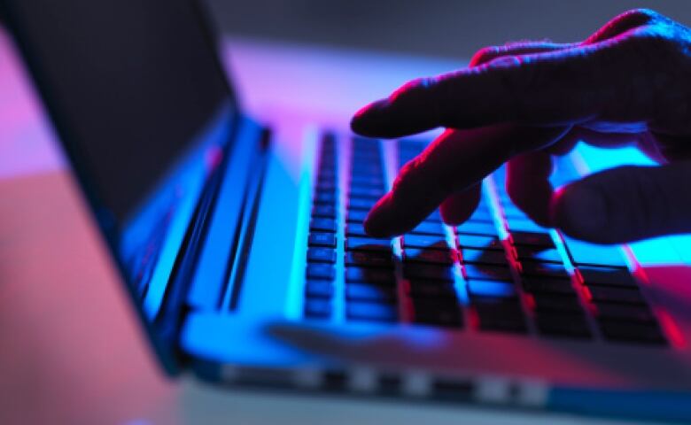 A hand types on a computer keyboard in a dark room.