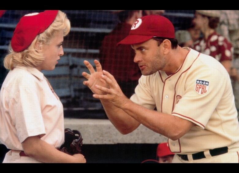 Tom Hanks and Bitty Schram are in a screengrab from the movie. In the scene, Hanks is gesturing at Schram in front of a baseball dugout.