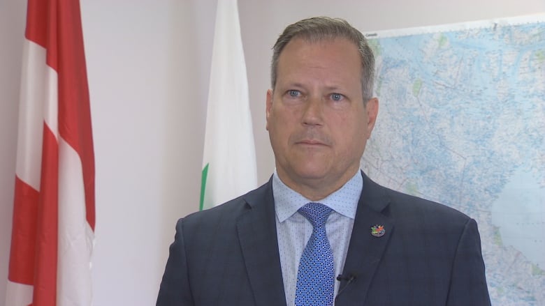 A man standing in a suit and tie with a Canada flag in the background.