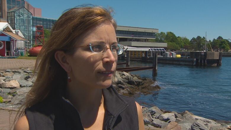 A woman with brown hair and glasses is shown with the Halifax harbour in the background.