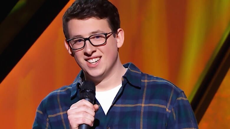 A young person in glasses and a plaid shirt holds a microphone.