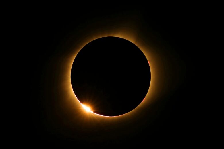 A black disk is surrounded by orange-yellow light.