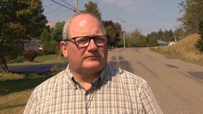 An unsmiling man standing outside in plaid shirt