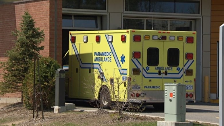 A yellow ambulance with blue writing is parked at a hospital on a sunny day.