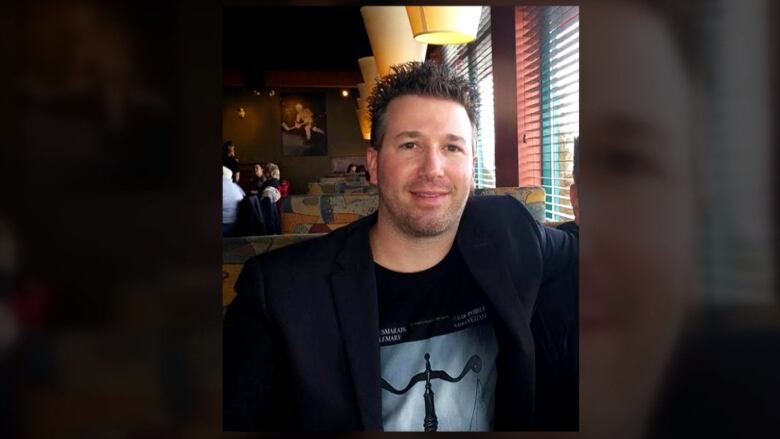 A man sits in a restaurant, smiling.