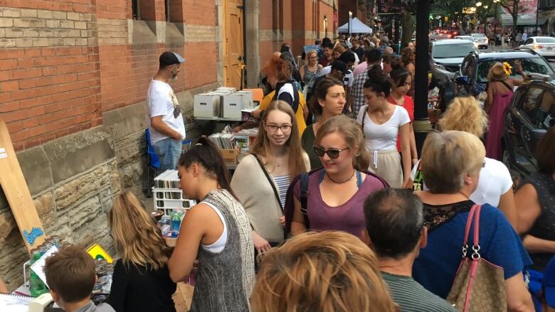 The sidewalk outside a large brick building is packed with people walking and selling art