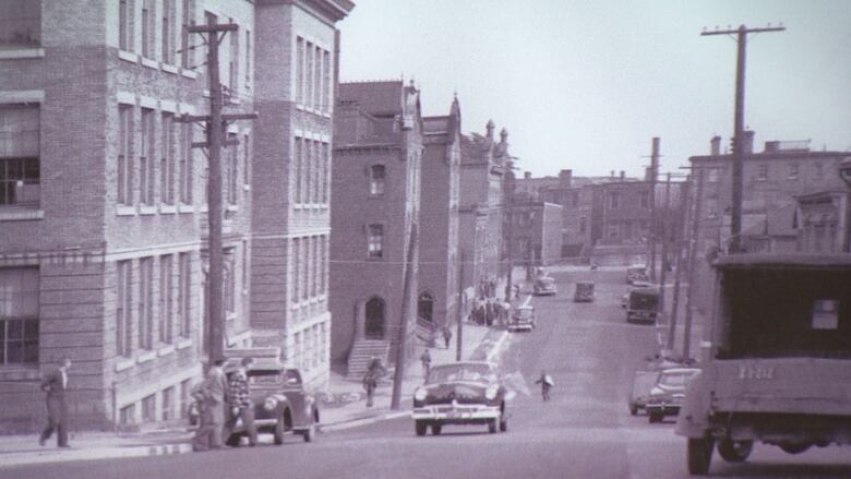 An old black and white photo of a city street lined with brick buildings. 