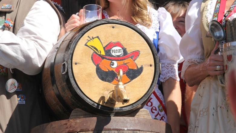 A wooden beer keg on its side with an orange cartoon face. The face of Onkl Hans is wearing a Bavarian hat with a feather